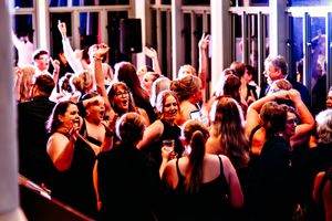 Wedding reception dance floor filled with guests dancing under colorful lighting.