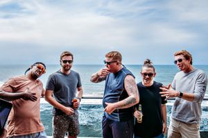 Group enjoying drinks and conversation by the ocean on a sunny day.