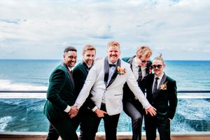 Wedding party posing together on a beach with ocean waves in background.