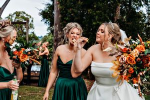 Wedding party members holding vibrant orange and white floral bouquets outdoors.