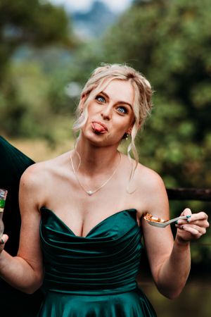 Person in emerald green dress making playful expressions during wedding photos.