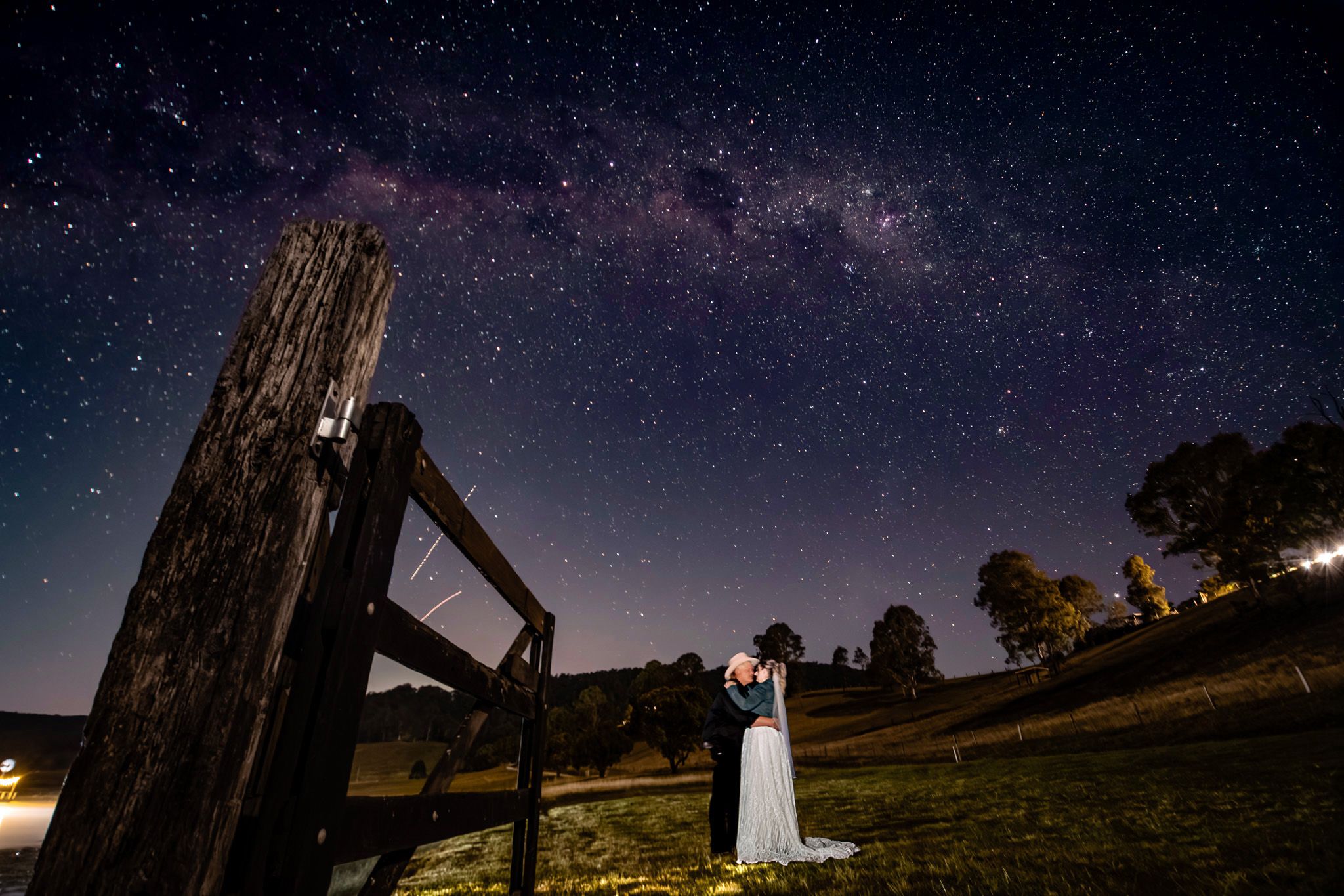A romantic nighttime wedding photo under the Milky Way galaxy with a rustic fence.