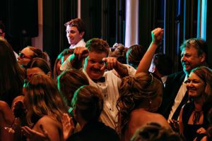 Energetic crowd celebrating and dancing at a dimly lit party or reception.