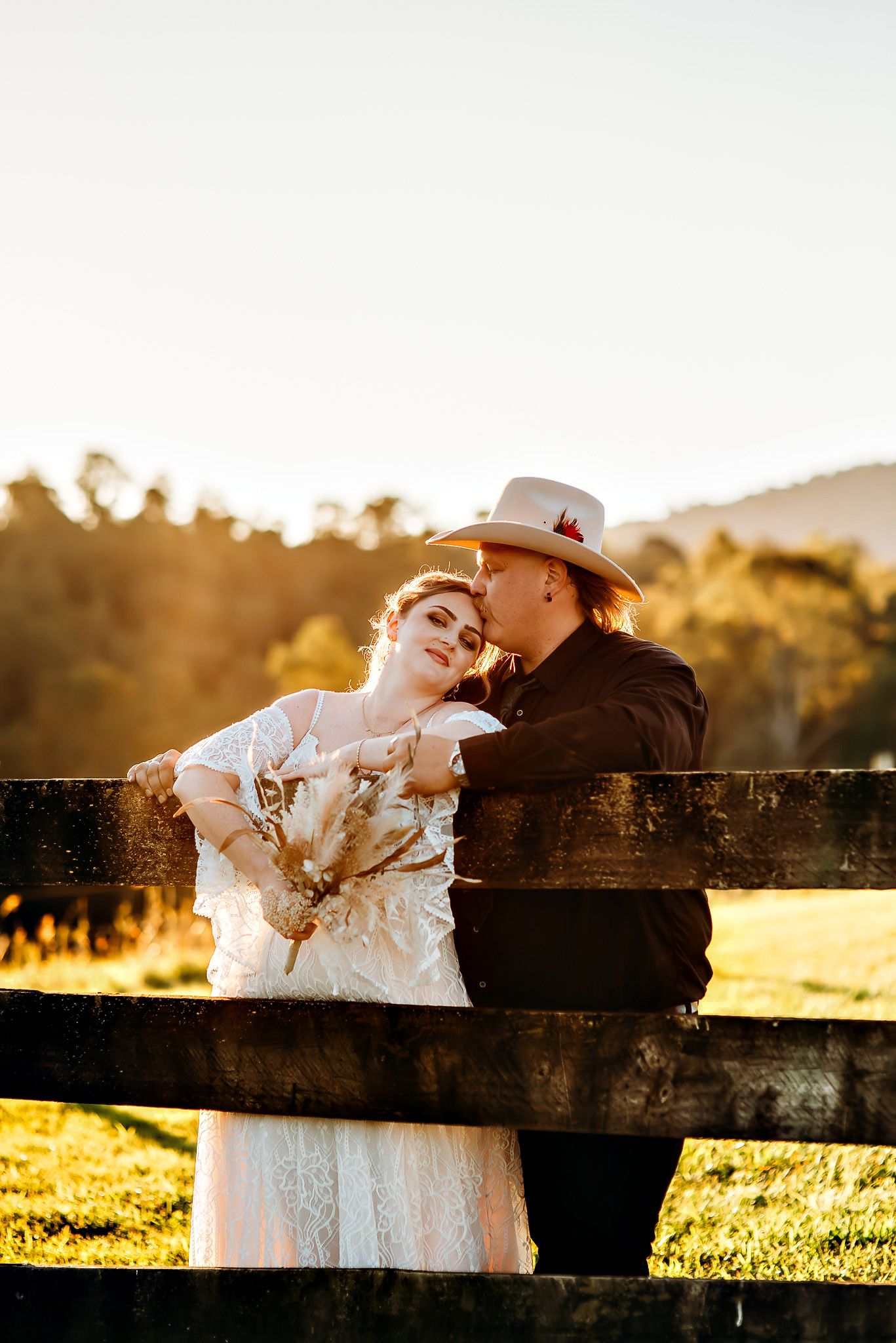 A couple shares an intimate moment leaning against a wooden fence at sunset.