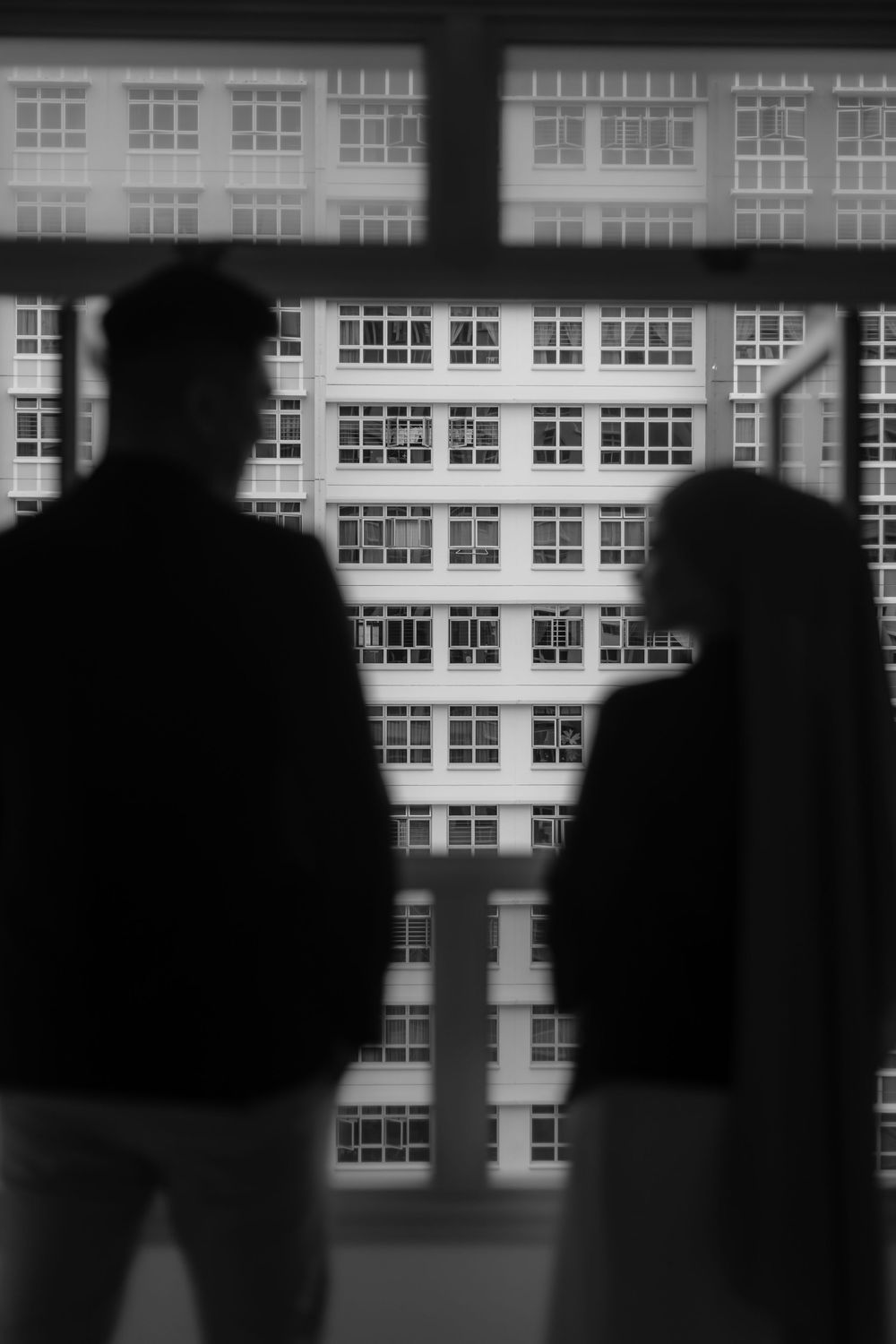 Black and white silhouettes of two people facing each other against a large window with a city building backdrop.