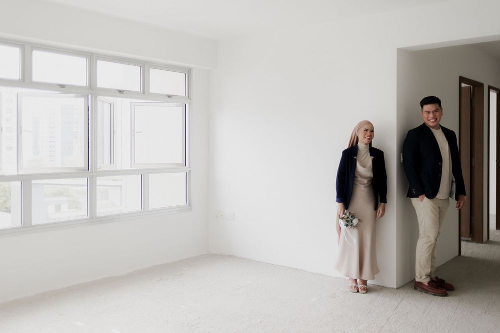 Couple standing in empty white apartment room with large windows and city view.