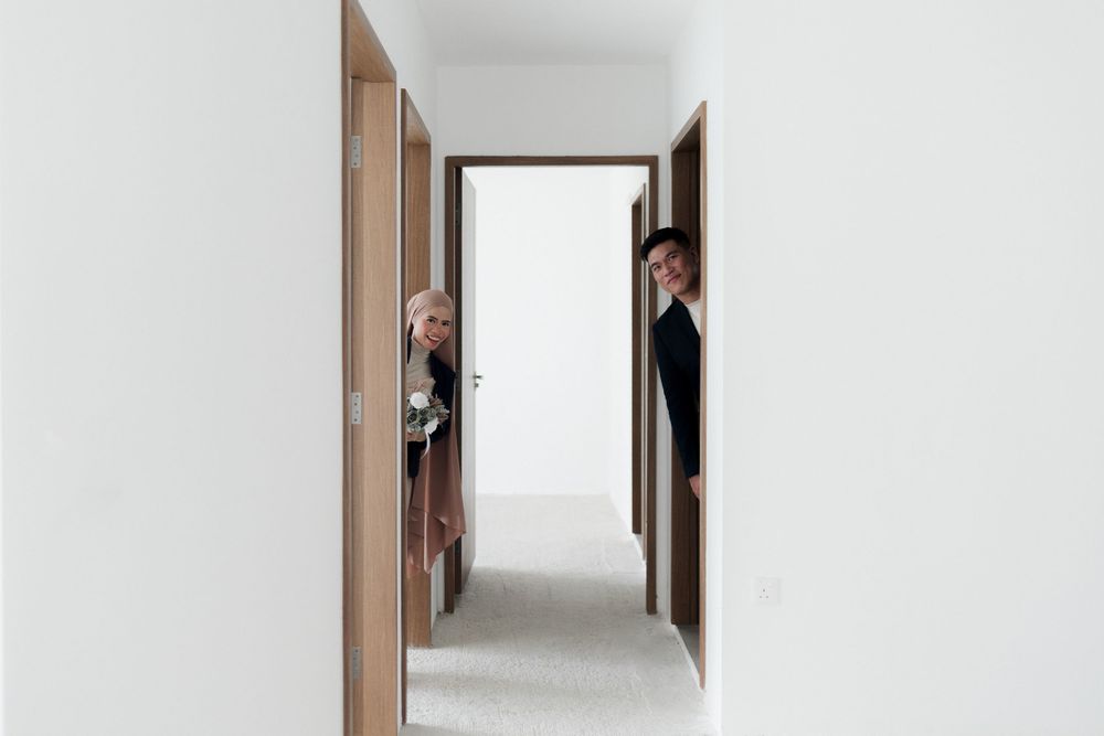 Two people playfully peek around wooden doors in a modern white hallway with minimalist interior design.