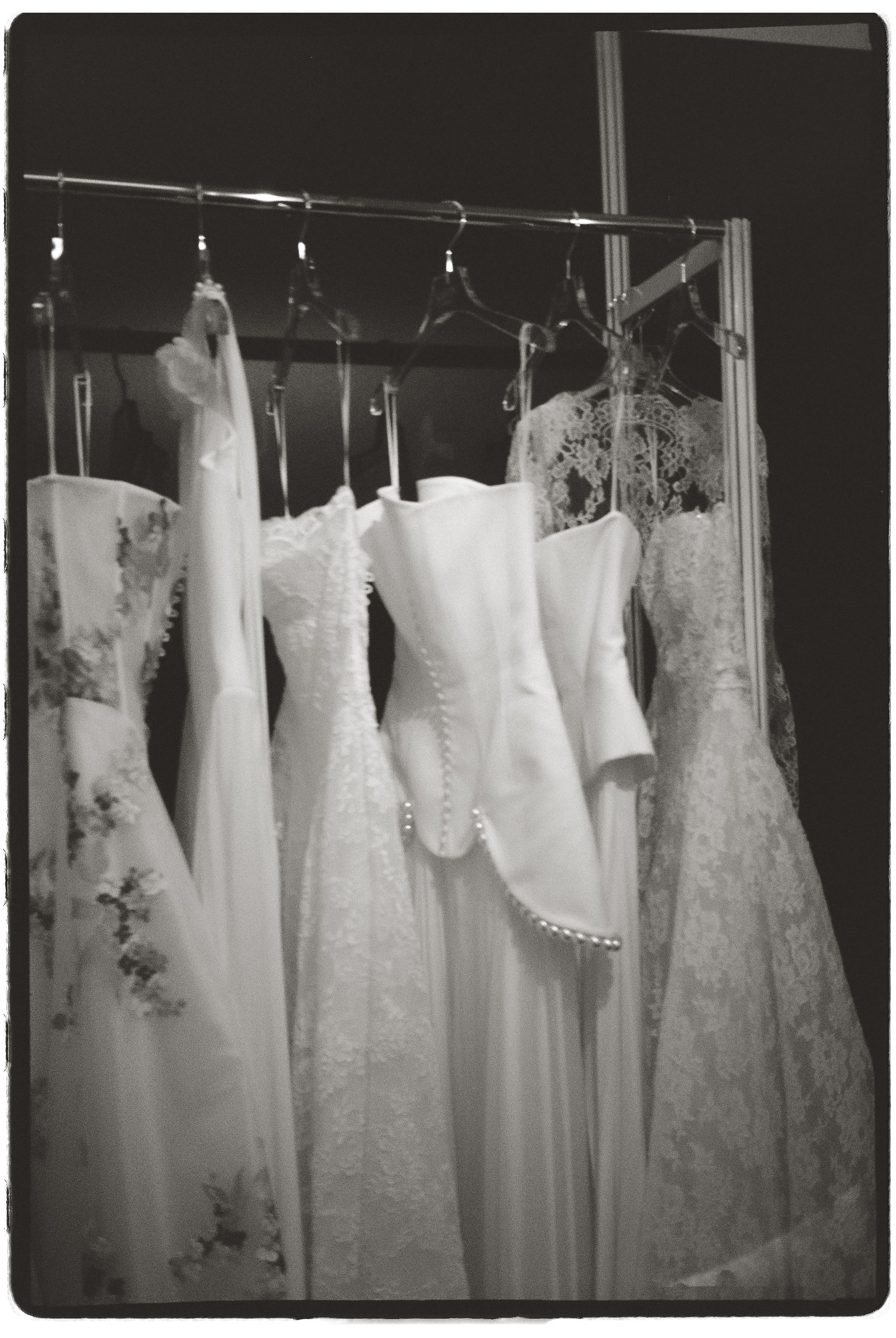 Black and white photo of elegant white wedding dresses hanging on a rack in a bridal boutique.
