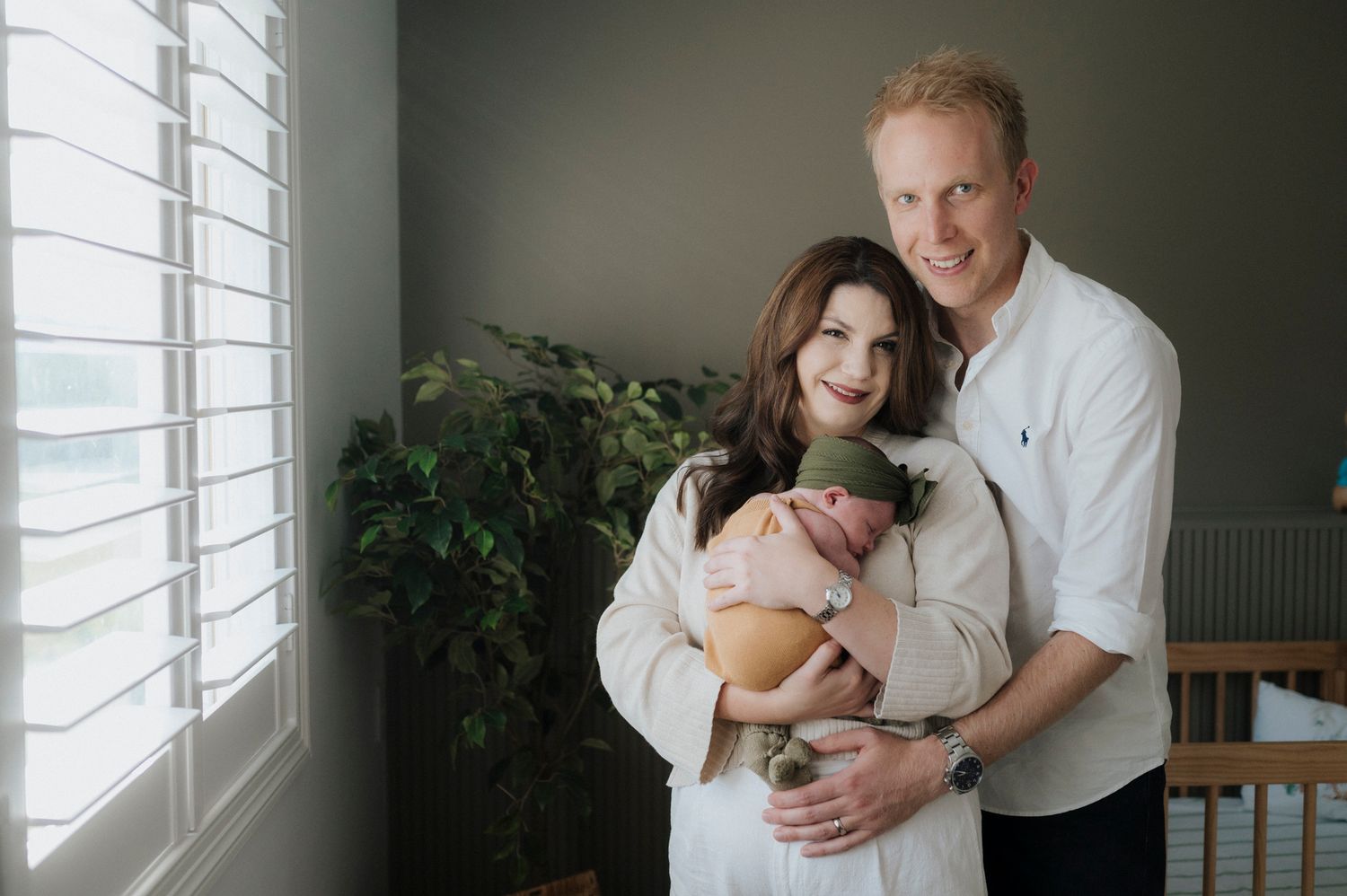 New parents smiling and holding their newborn baby in a cozy nursery room with natural light.