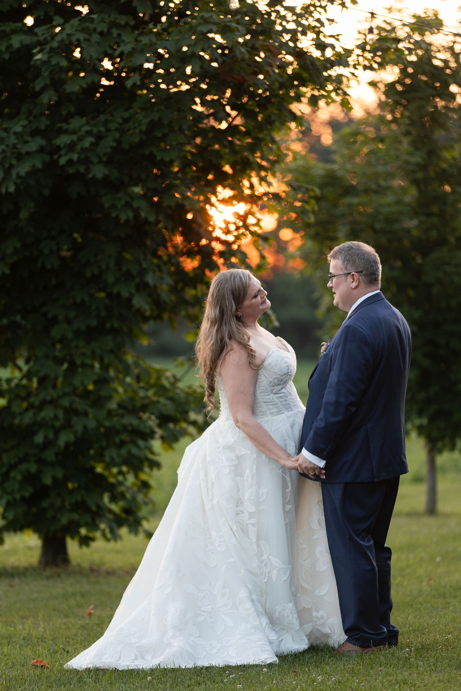Bride and groom hold hands at golden hour sunset, surrounded by lush green trees at barn swallow fields in guelph, ontario.