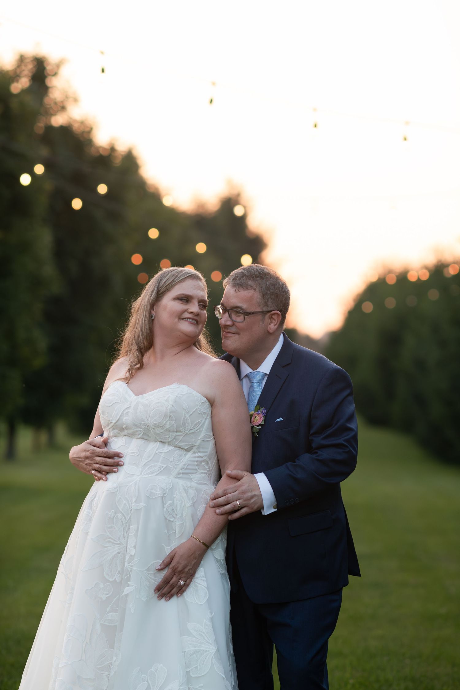 Bride and groom embrace at sunset in an orchard with string lights at barn swallow fields in guelph, ontario.