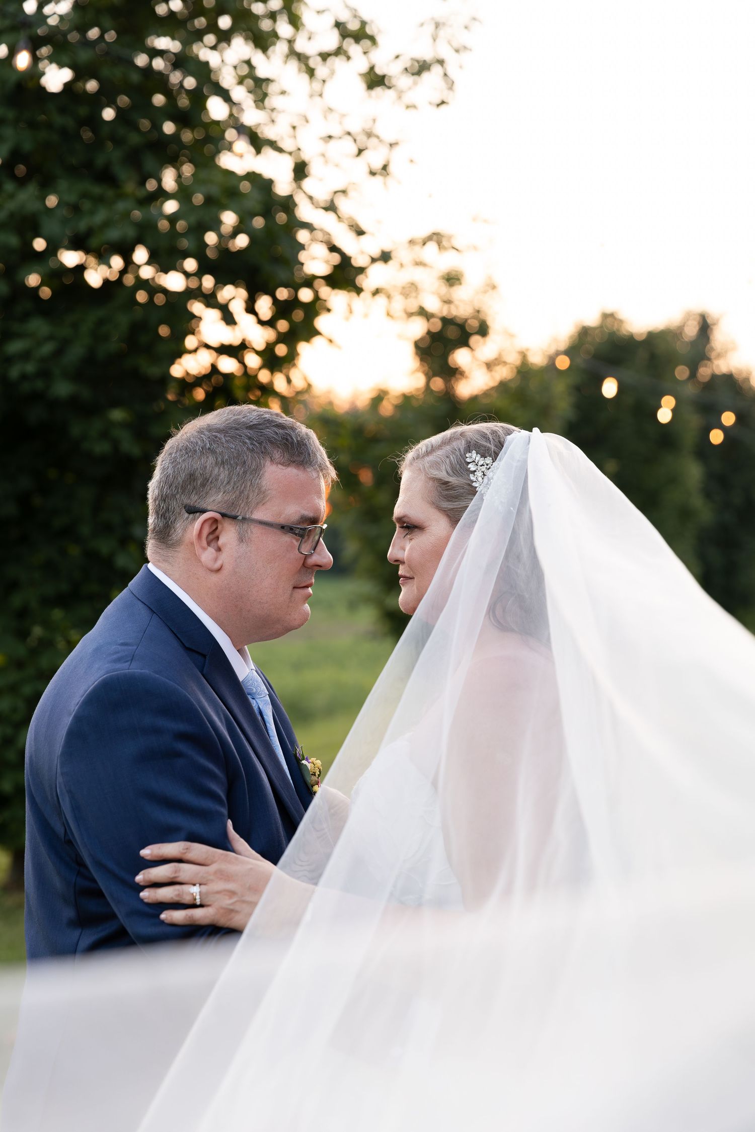 Bride in white veil and groom in blue suit share a tender moment outdoors at golden hour wedding at barn swallow fields in guelph, ontario.