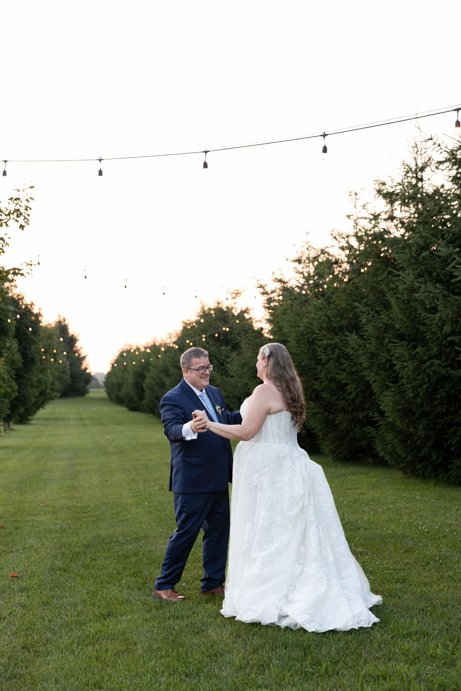 Bride and groom share first dance outdoors on lush green lawn at dusk with string lights at barn swallow fields in guelph, ontario.