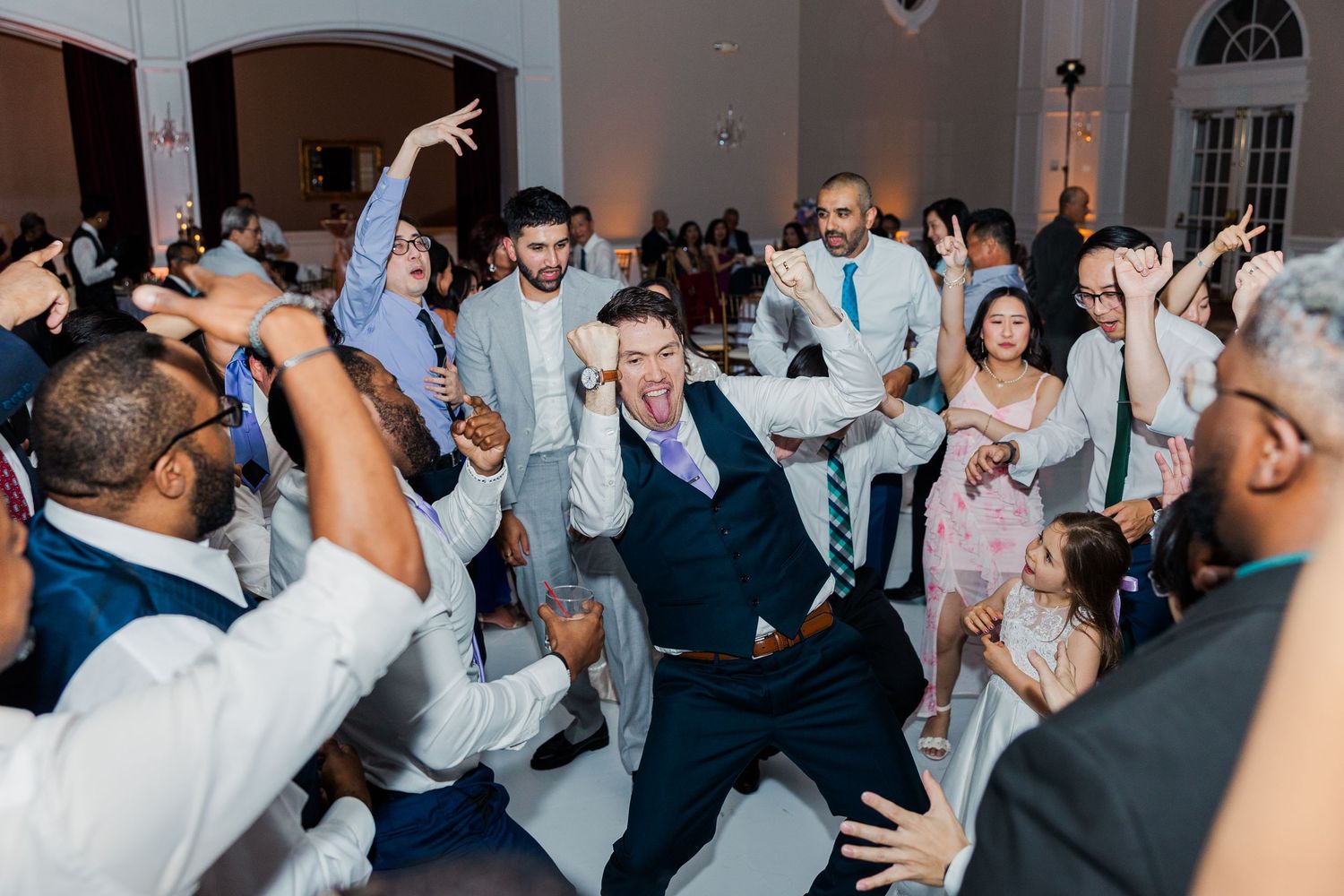 Guests dancing energetically at a lively wedding reception in an elegant white ballroom.