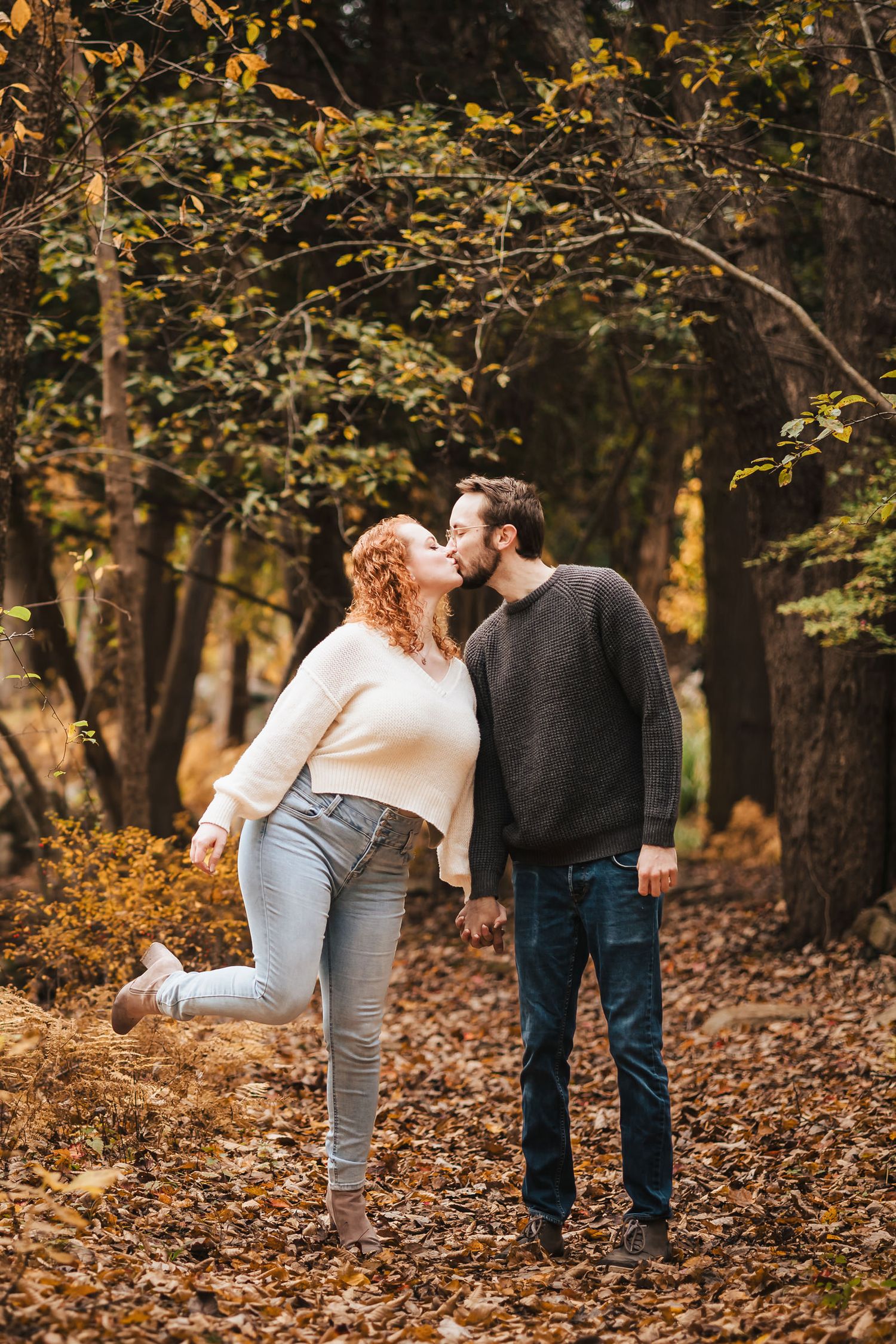 Engaged couple kissing in the forest at Borderland State Park, her foot kicked up playfully behind her.