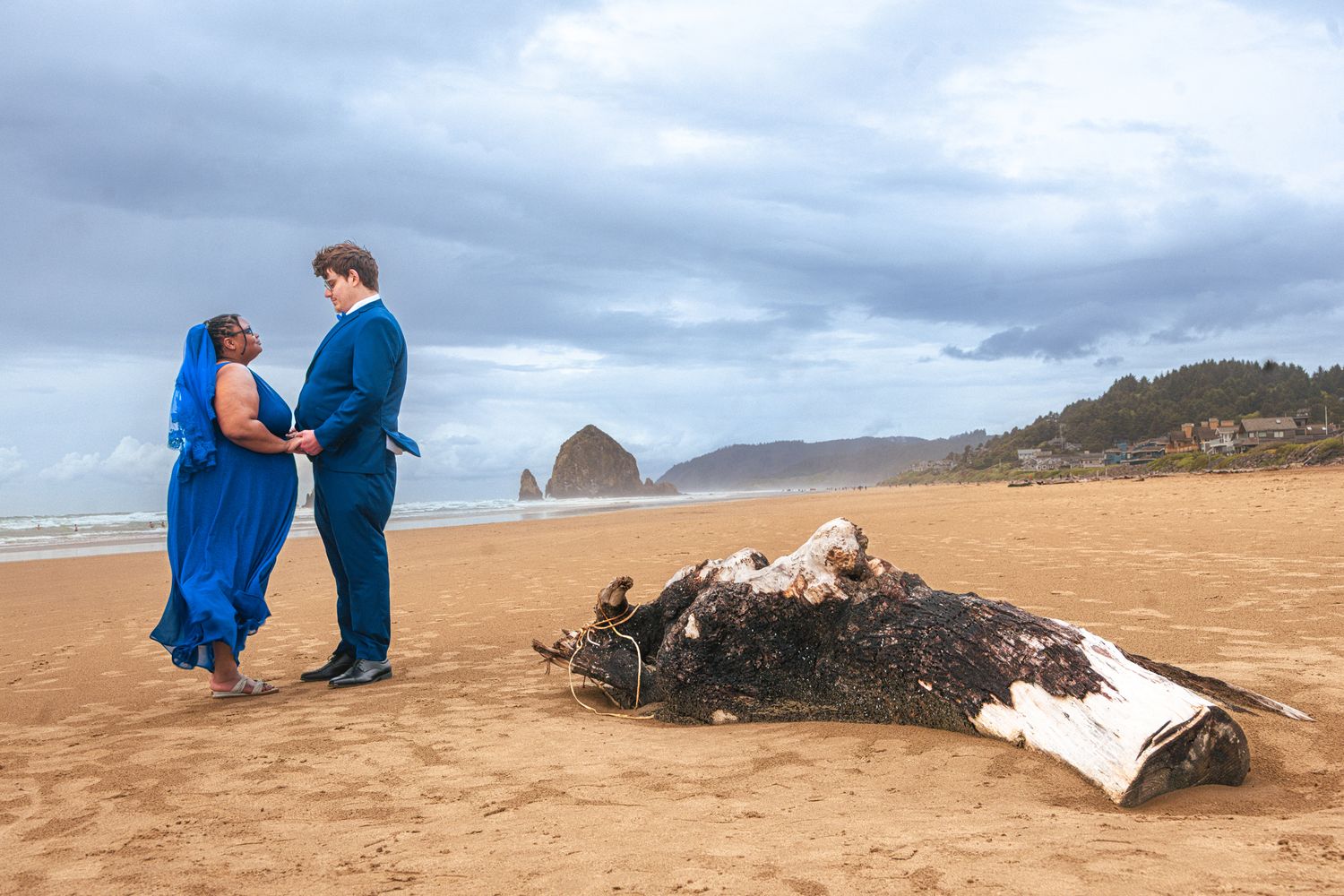 Couple in blue attire sharing a romantic moment on Cannon Beach with Haystack Rock in the background.