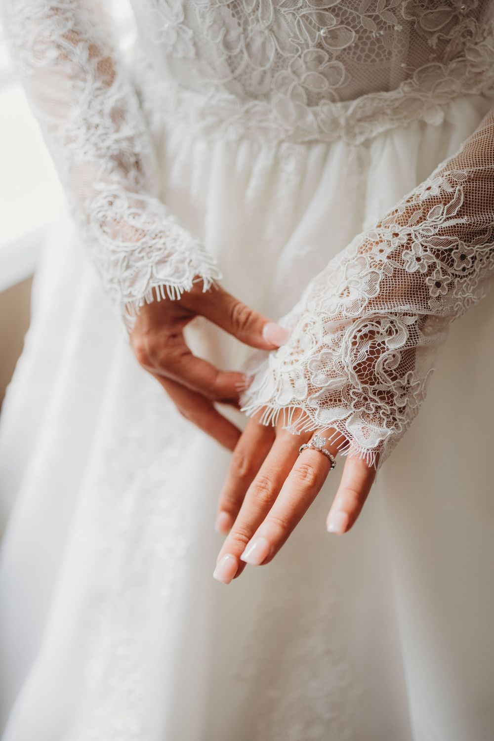 Bride in lace wedding dress with sheer gloves, showcasing elegant ring on finger.