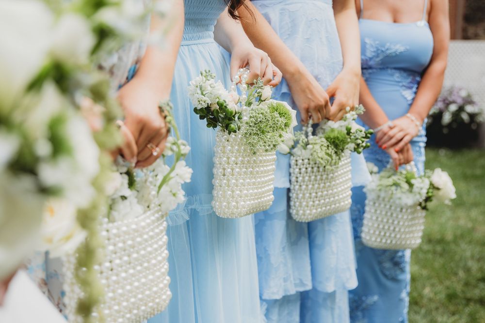 Bridesmaids in light blue dresses holding white pearl beaded bags filled with green and white flowers.
