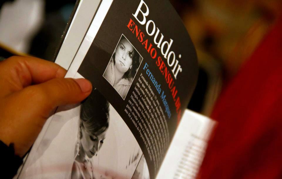 A hand holds a Boudoir book with a woman's photo on the cover at a literary event.