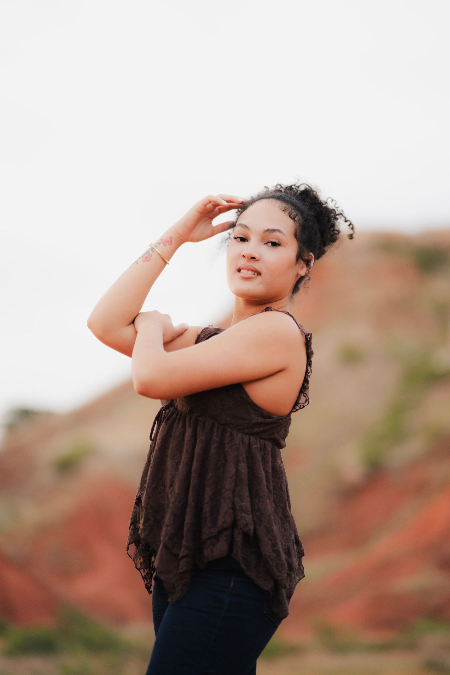 Young woman in dark floral top poses confidently outdoors with red rock formations in background.