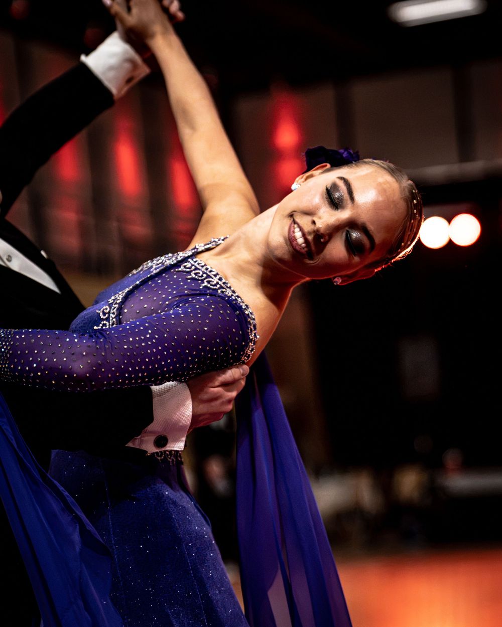 Elegant ballroom dancers in blue rhinestone costume perform a dramatic dip at a competitive dance event.