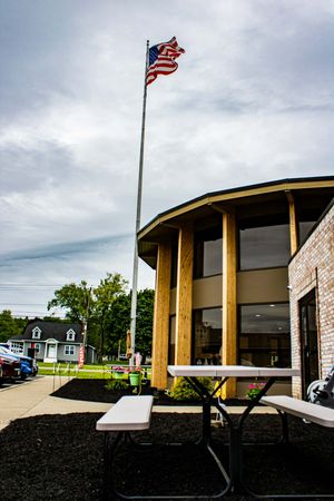 American flag flying on tall flagpole outside a modern brick building with wooden columns and picnic table.