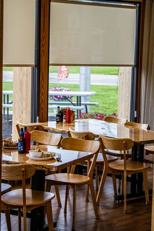 Bright casual restaurant dining area with wooden chairs and tables near large windows overlooking a green lawn.