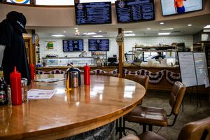 Interior of a classic American diner with wooden tables, condiments, and digital menu boards above the counter.