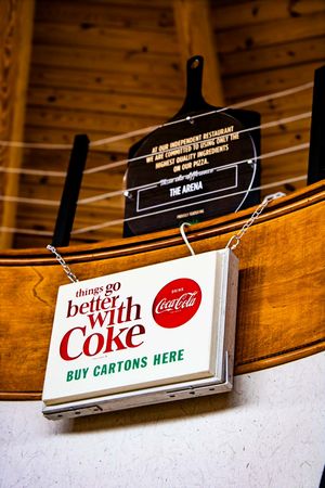 Vintage Coca-Cola sign reading things go better with Coke buy cartons here hanging in a rustic restaurant.