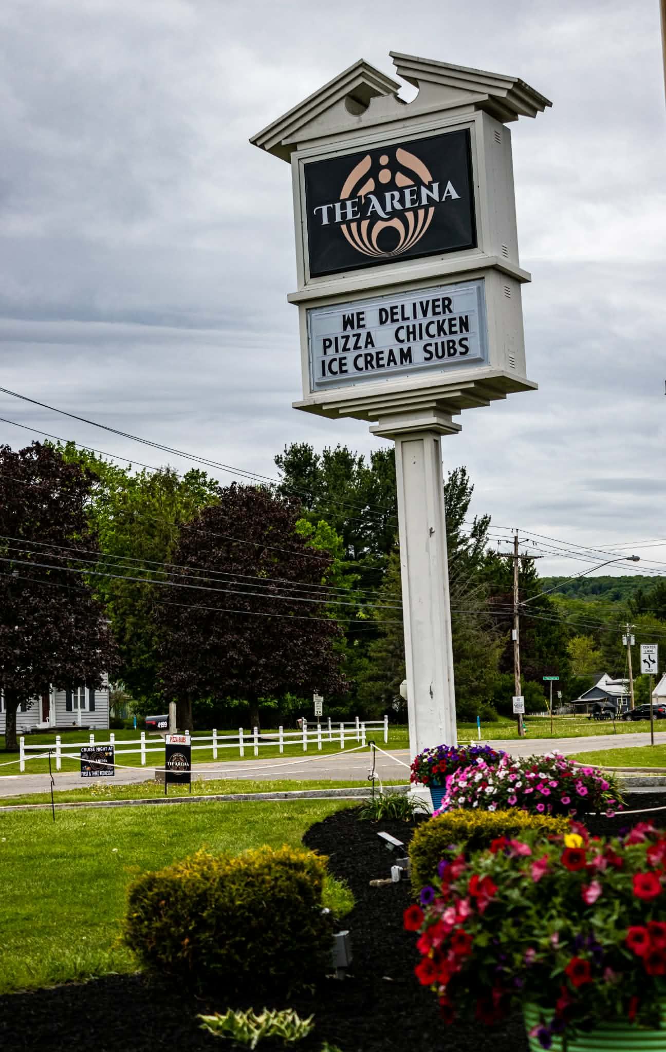 Tie Arena restaurant sign advertising pizza, chicken, ice cream, and subs delivery service, surrounded by colorful flowers.