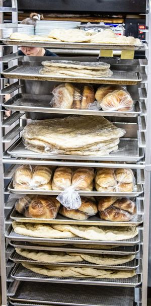 Commercial bakery rack filled with fresh bread loaves and flatbreads on metal trays in a professional kitchen.