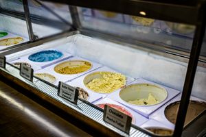 Glass display case showcasing various gelato flavors in metal pans at an ice cream shop.