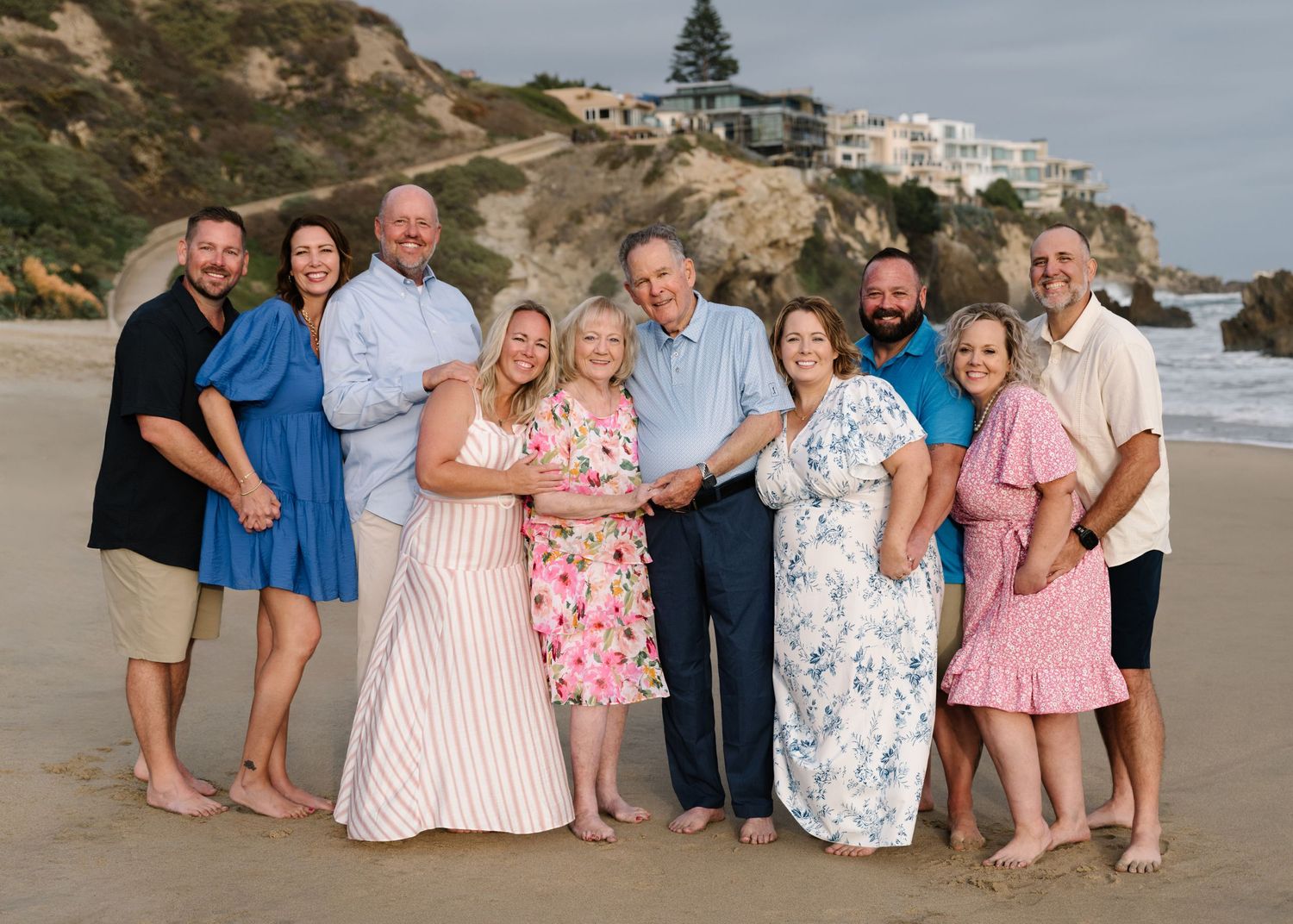 Large extended family gathered together on the beach with Newport Beach cliffs in the background.