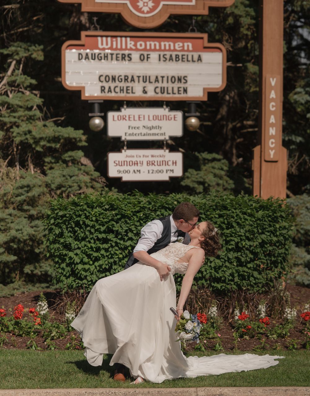 Bride and groom share a romantic dip kiss in front of a Willkommen sign congratulating Rachel and Cullen.