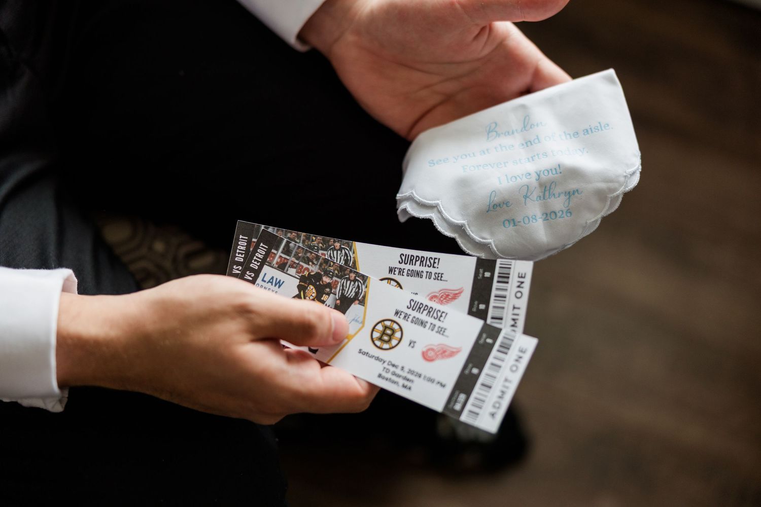 Hands holding Boston Bruins and Detroit Red Wings hockey tickets with a white napkin at a wedding.