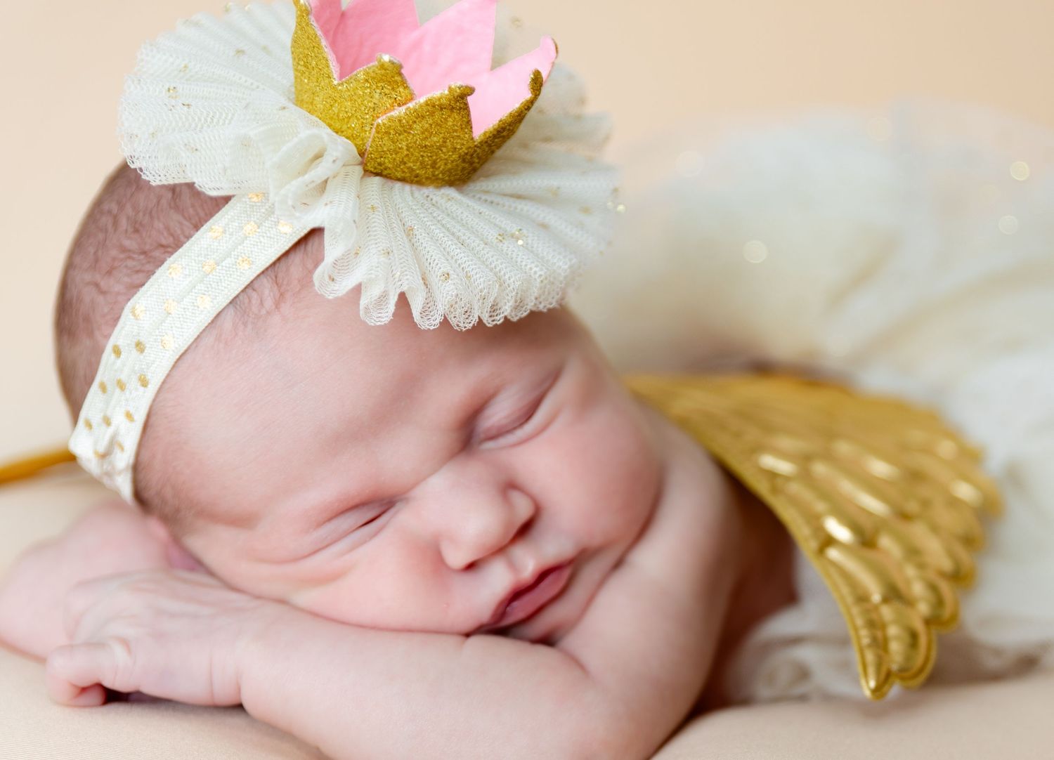 newborn photographer Calhoun GA, Sleeping newborn baby wearing a gold and pink crown headband with white ruffles and gold angel wings.