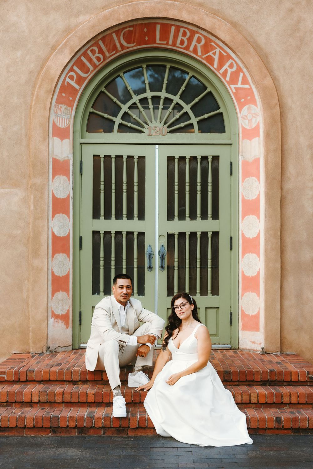 Bride and groom posing on brick steps in front of a decorative Public Library arched doorway.