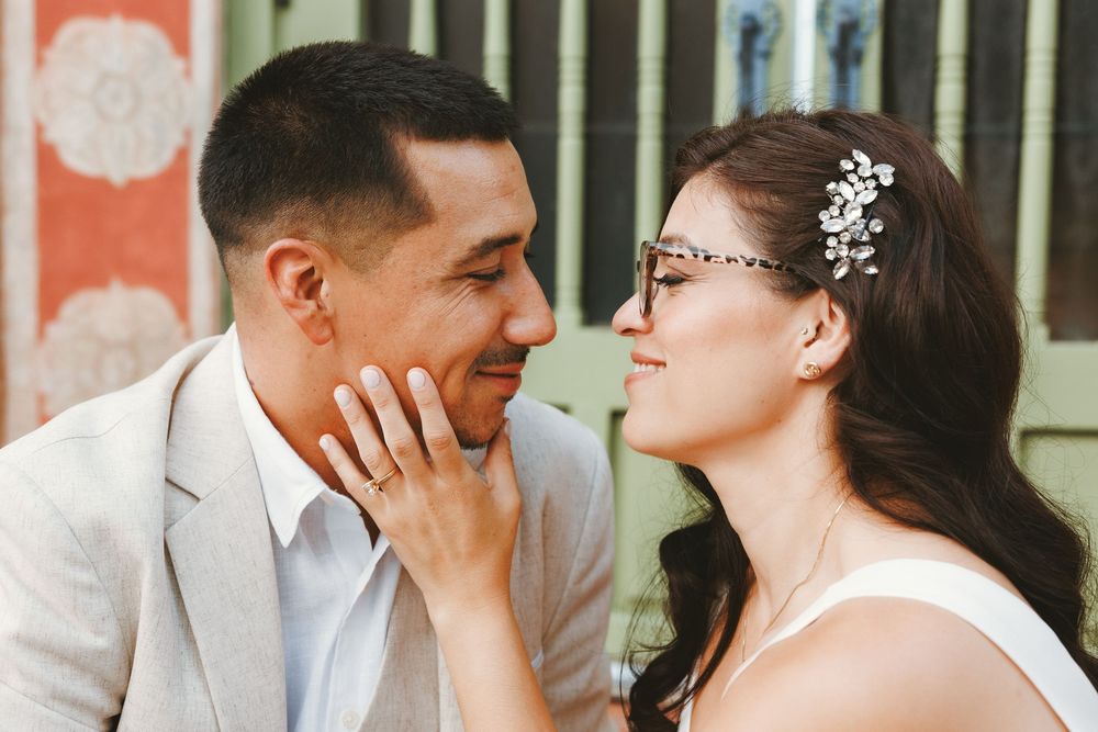 A bride and groom share a tender moment, smiling at each other, with the bride wearing a floral hair accessory.