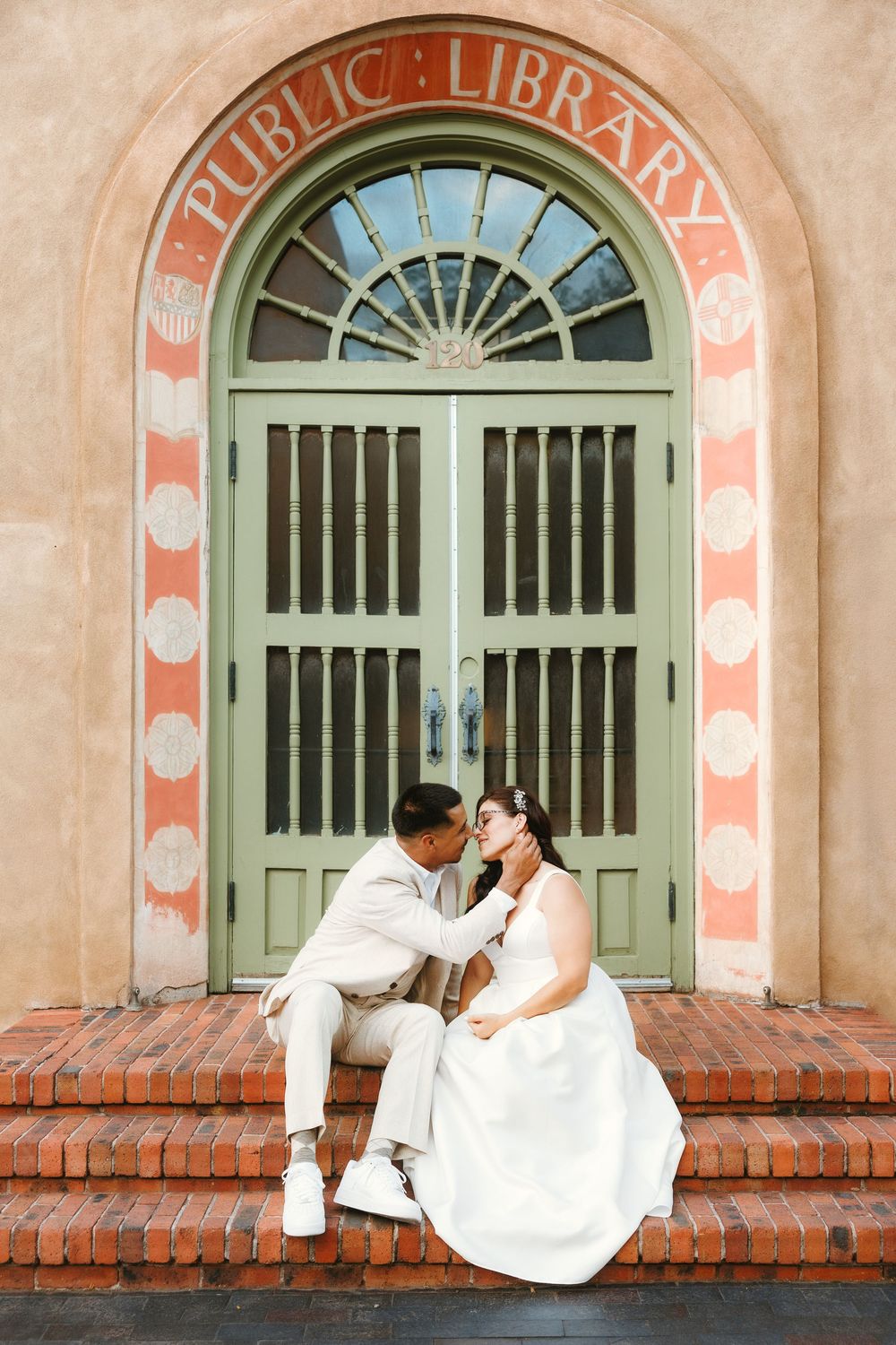 Bride and groom share a tender moment on brick steps of a Public Library in their wedding attire.