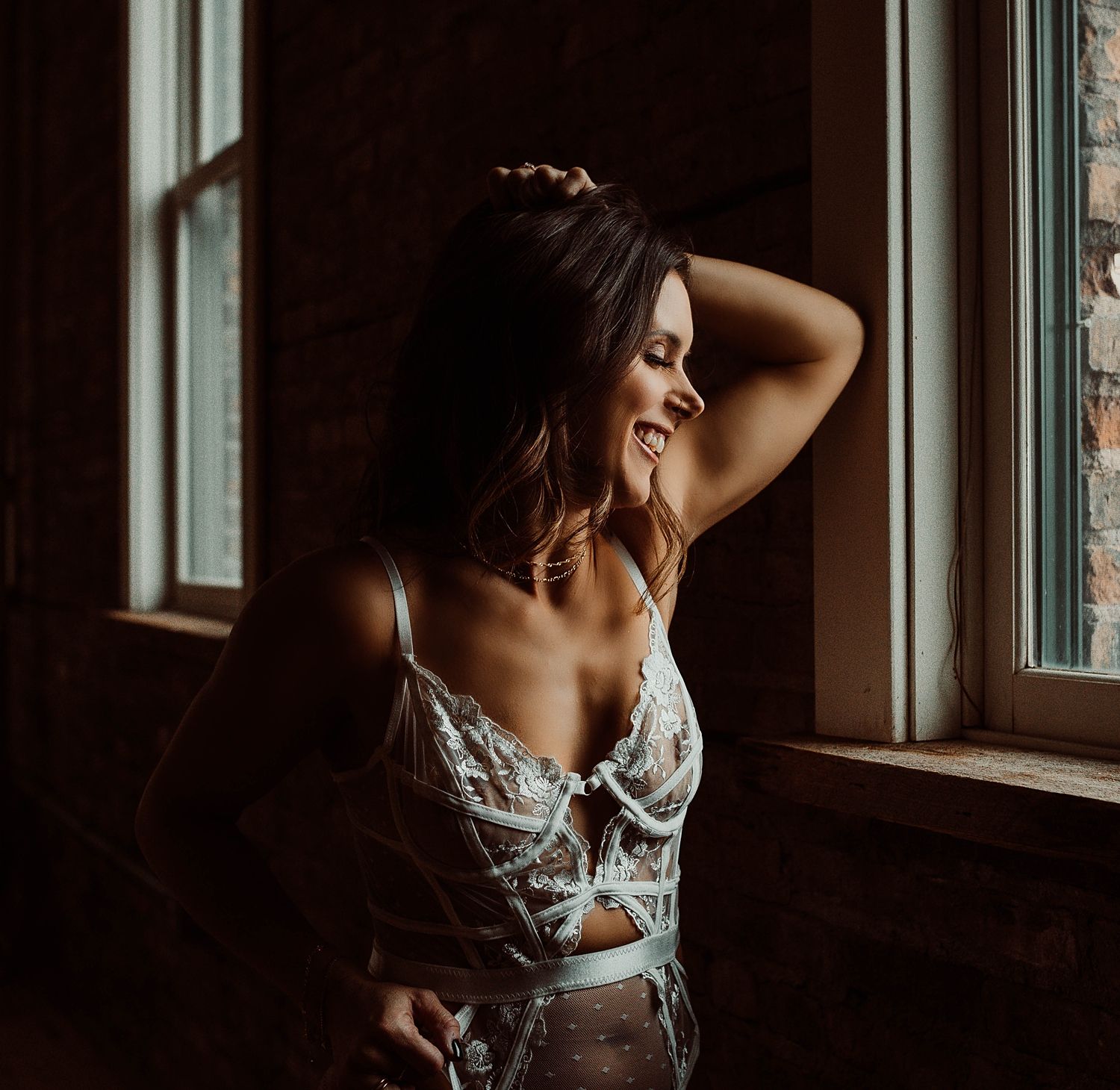 brunette in lace bodysuit by a window for non-traditional bridal boudoir photoshoot