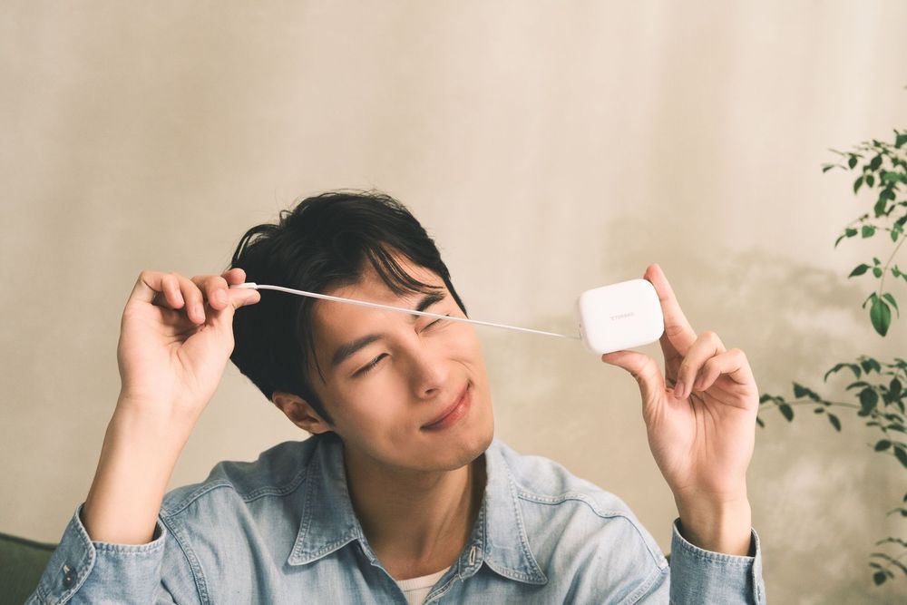 Young man holding dental floss near his hair with eyes closed, enjoying a self-care routine indoors.