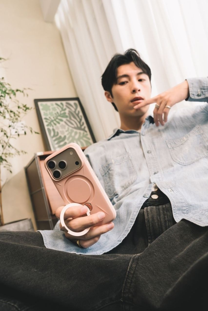 Young man holding a pink iPhone case with MagSafe ring holder while sitting on a couch indoors.