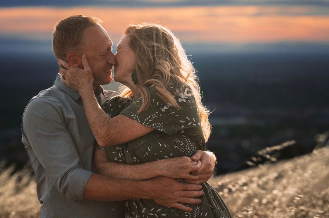 Couple embracing and kissing at sunset on a hilltop with scenic landscape views in golden hour light.
