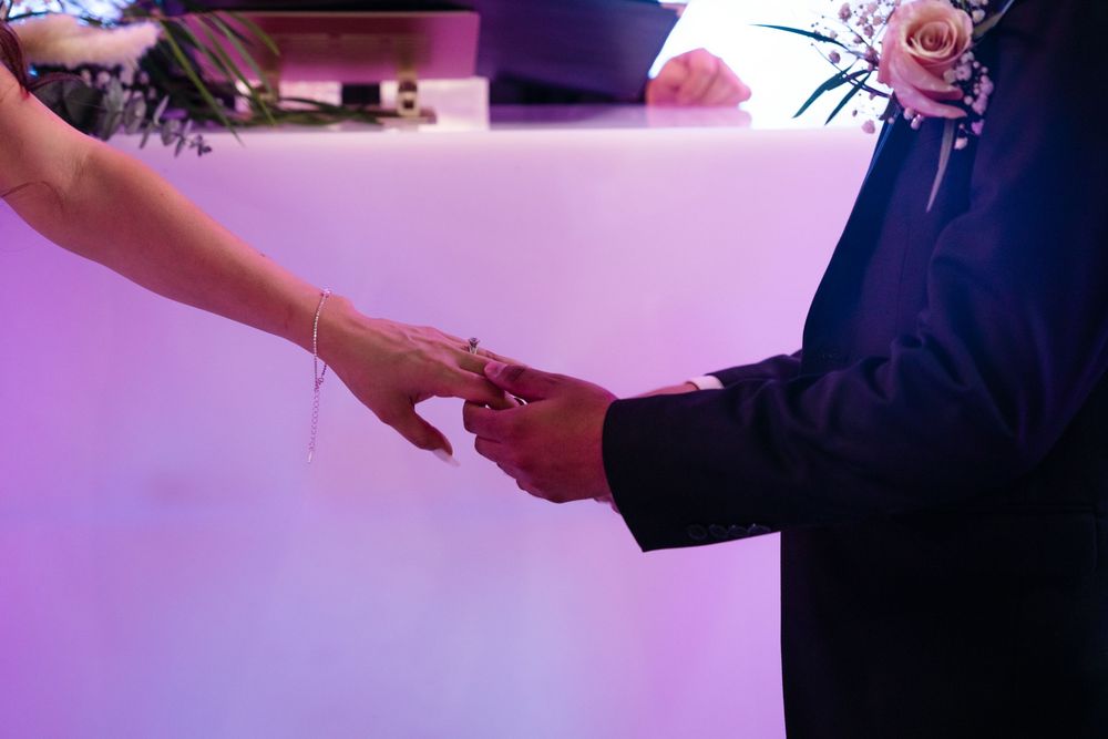 Bride and groom exchanging rings at wedding ceremony with purple ambient lighting.