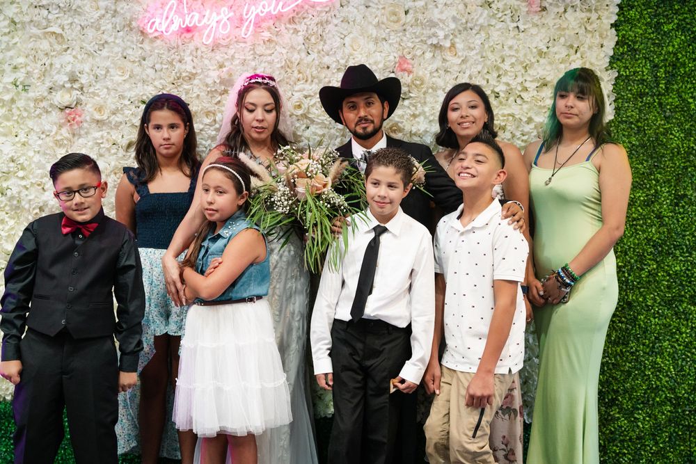 Family group photo at a formal event with floral backdrop, adults and children dressed in elegant attire.
