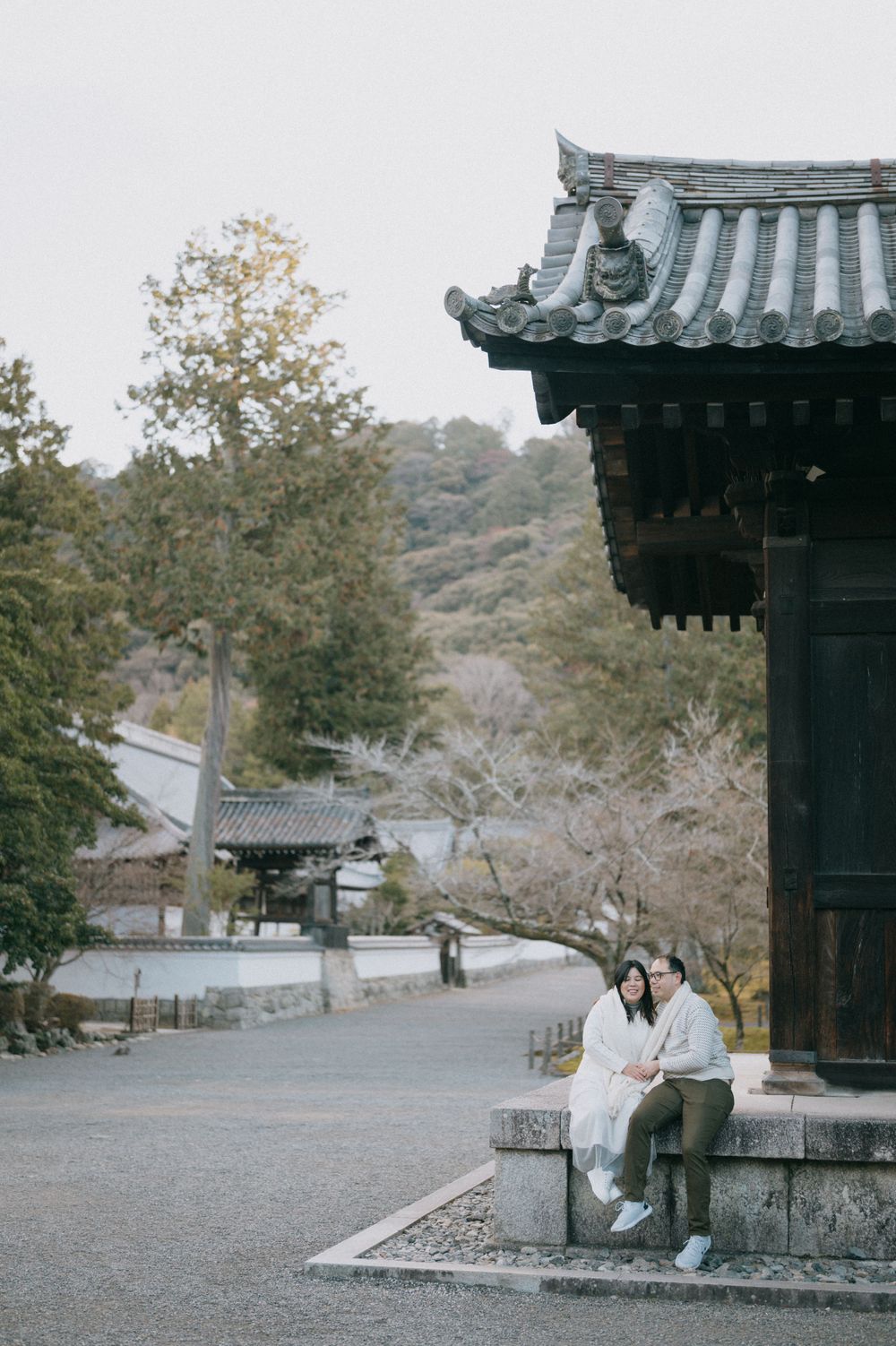 Couple sitting together on stone base beside traditional Japanese pagoda in serene temple garden.