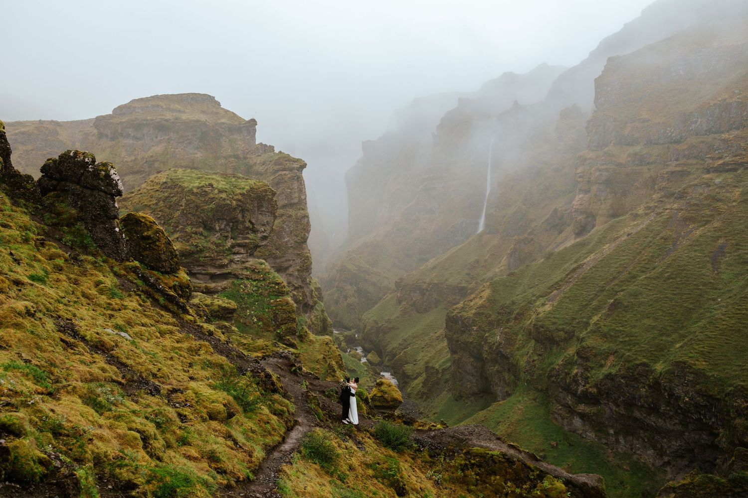 brides kissing with a view of a waterfall and canyon at Mulagljufur Canyon during their Iceland elopement