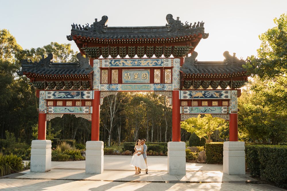 Couple embracing under ornate red Chinese ceremonial gate in a sunlit park photoshoot in nurragingy reserve