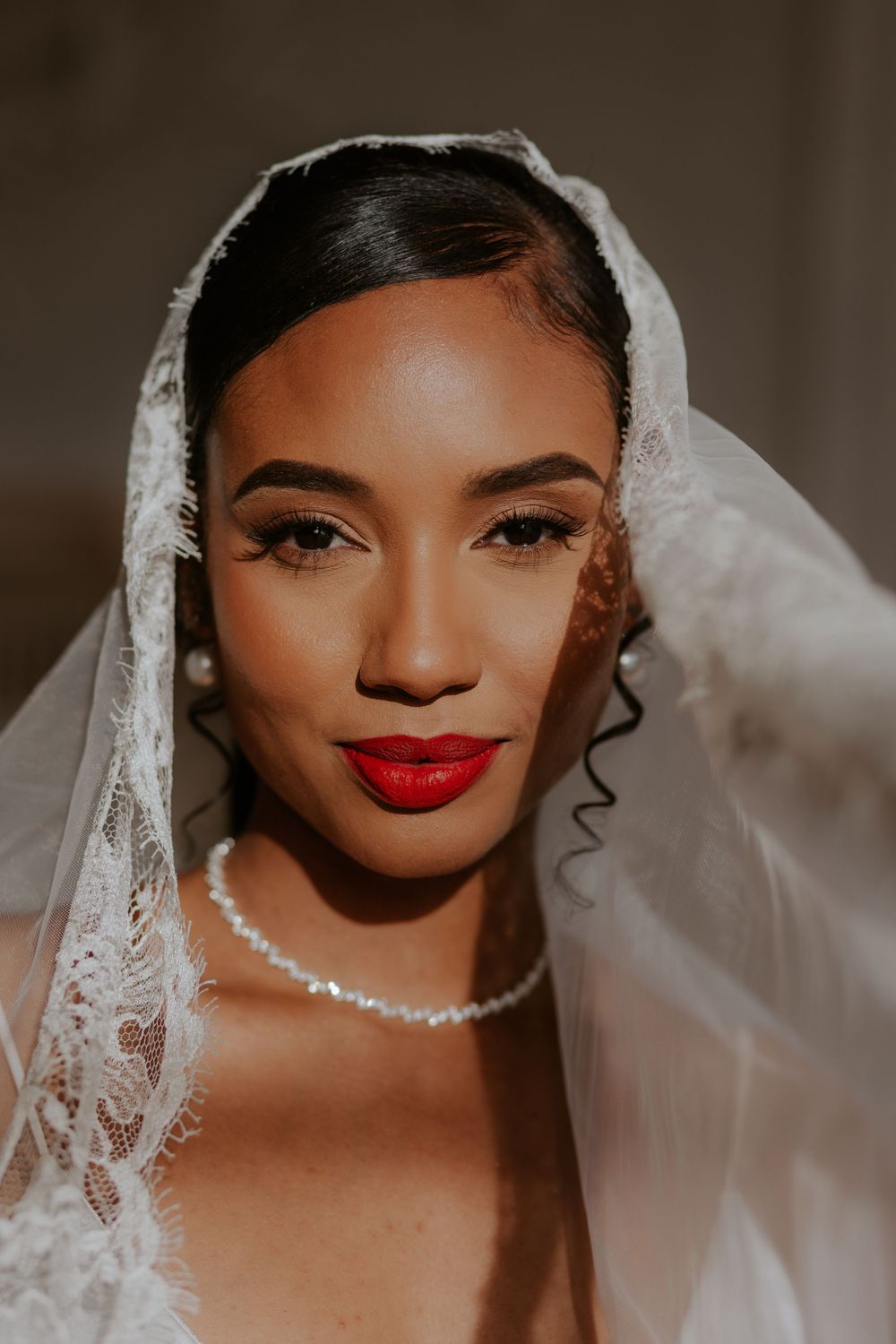 A close-up portrait of a bride wearing a delicate veil and red lipstick.
