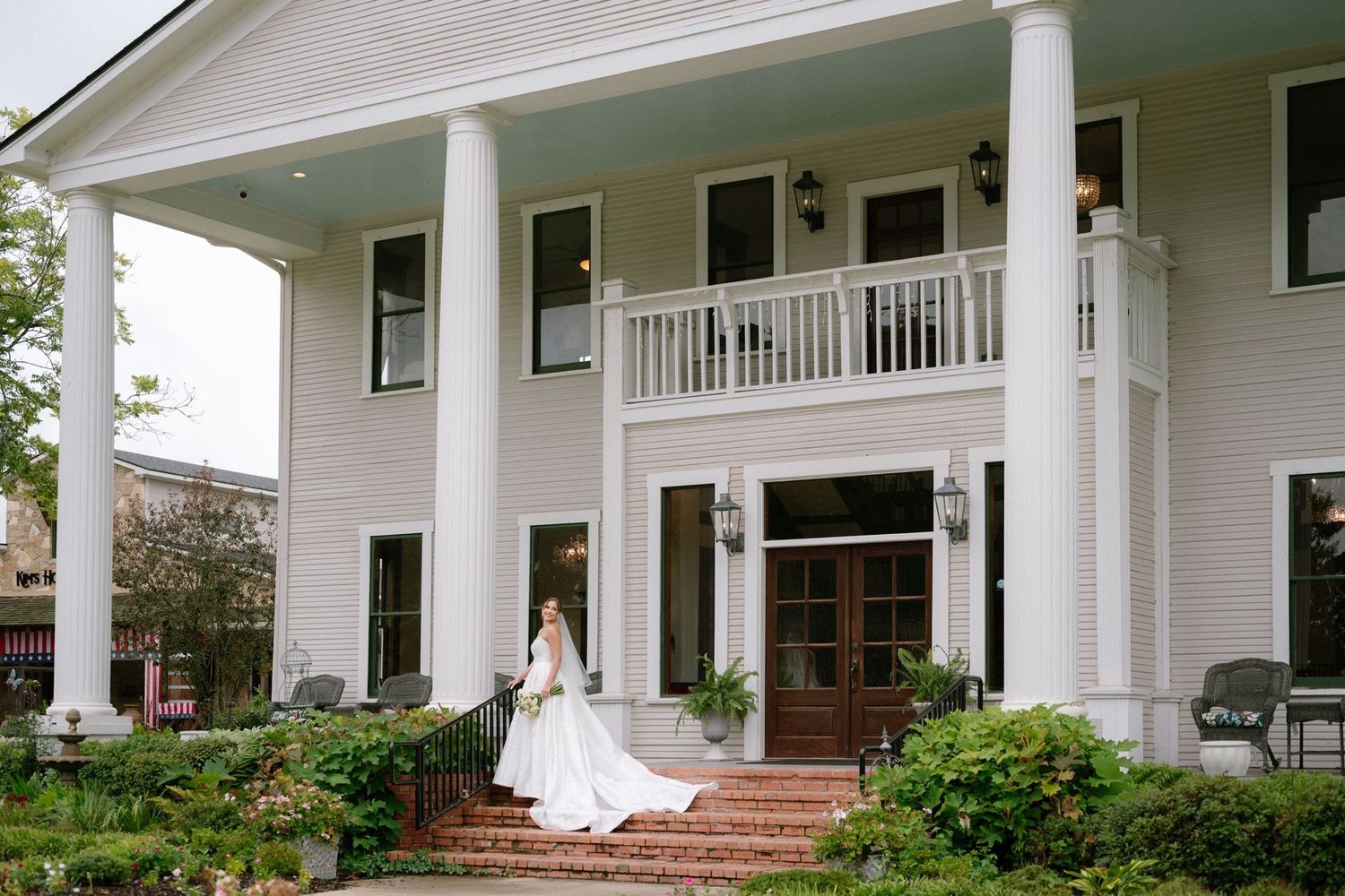 Bride in a strapless white ball gown sits gracefully on a black Chiavari chair, gazing toward a window in soft natural light.